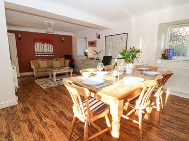 A dining table with six chairs set with plates and glasses next to a sitting area with a sofa and coffee table at Stone Wheel Cottage in Hook Norton