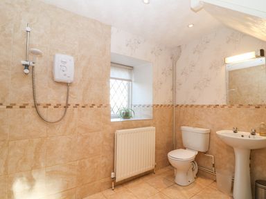 A bathroom with a shower, toilet, pedestal sink, radiator, window with a plant and a mirror at Stone Wheel Cottage in Hook Norton