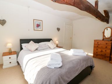 A bedroom with a large bed with pillows and folded towels bedside tables with lamps a wooden dresser with a mirror and exposed wooden ceiling beams at Stone Wheel Cottage in Hook Norton