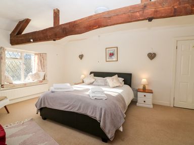 A bedroom with a bed window seat bedside tables and wooden ceiling beam at Stone Wheel Cottage in Hook Norton
