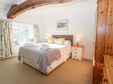 A bedroom with a double bed bedside tables lamps wooden wardrobe and window with floral curtains at Stone Wheel Cottage in Hook Norton
