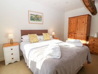 A bedroom with a double bed two yellow pillows two bedside tables with lamps a wooden wardrobe and a chest of drawers at Stone Wheel Cottage in Hook Norton