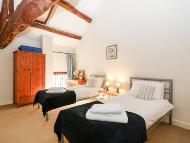A bedroom with two single beds a wooden wardrobe and a desk at Stone Wheel Cottage in Hook Norton