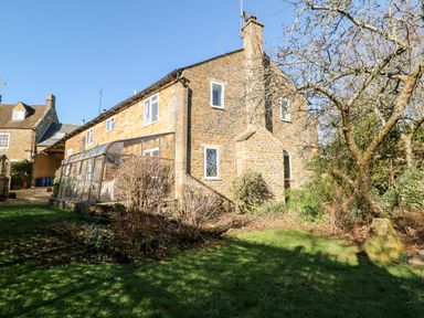 A stone house with a glass greenhouse structure and garden at Stone Wheel Cottage in Hook Norton