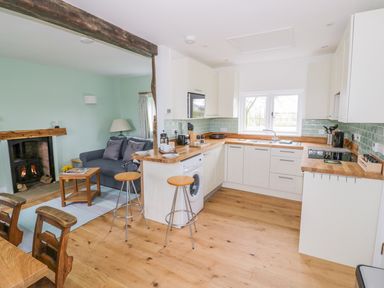 A kitchen with white cabinets and wooden countertops next to a living area with a sofa and fireplace at Wigrams Canalside Cottage in Napton-on-the-Hill