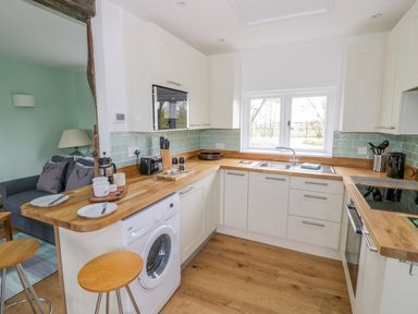 A kitchen with white cabinets wooden countertops a washing machine stools and a window at Wigrams Canalside Cottage in Napton-on-the-Hill