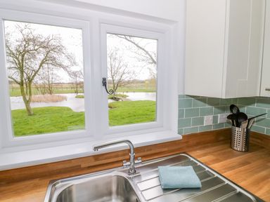 A kitchen sink with a faucet and a blue cloth on the countertop near a window showing a green lawn and trees at Wigrams Canalside Cottage in Napton-on-the-Hill