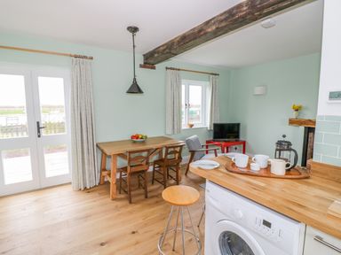 A kitchen dining area with a wooden table and chairs a stool a small television on a red stand and a washing machine at Wigrams Canalside Cottage Napton-on-the-Hill