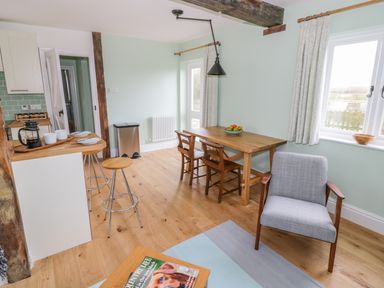A dining area with wooden table and chairs and a kitchen counter with stools and coffee cups at Wigrams Canalside Cottage Napton-on-the-Hill