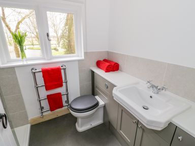 A bathroom with a toilet a sink red towels on a rail and countertop and a window with a vase of flowers at Wigrams Canalside Cottage in Napton-on-the-Hill