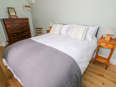 A bedroom with a double bed a wooden chest of drawers two bedside tables lamps and a wooden chair at Wigrams Canalside Cottage in Napton-on-the-Hill