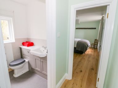 A bathroom with a toilet and sink next to a bedroom with a bed and wooden chair at Wigrams Canalside Cottage in Napton-on-the-Hill