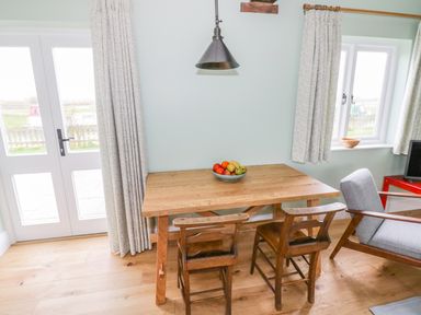 A dining area with a wooden table two wooden chairs a bowl of fruit a pendant light and windows with curtains at Wigrams Canalside Cottage in Napton-on-the-Hill