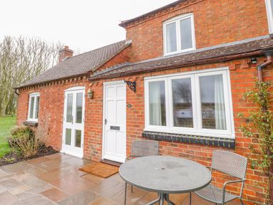 A patio with a round metal table and two chairs outside a red brick house at Wigrams Canalside Cottage in Napton-on-the-Hill