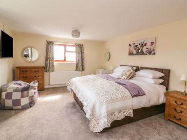 A bedroom with a double bed a chest of drawers a bean bag and a wall-mounted television at Treboeth in Knighton