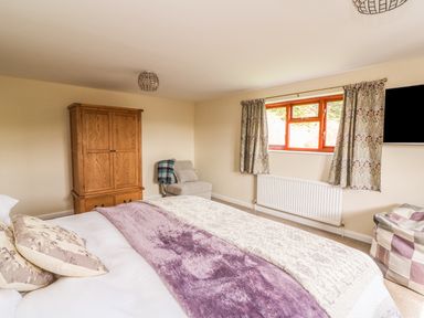A bedroom with a wooden wardrobe a fabric chair a window with curtains and a bed with pillows and blankets at Treboeth in Knighton
