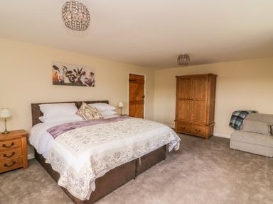 A bedroom with a bed bedside tables wardrobe armchair and animal painting on the wall at Treboeth in Knighton