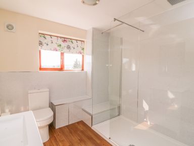 A bathroom with a toilet shower with glass divider wooden floor and window with floral blind at Treboeth in Knighton