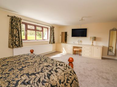 A bedroom with patterned bedspread curtains a wall-mounted TV and a dresser with a stool and mirror at Treboeth in Knighton