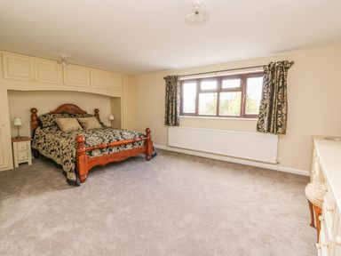 A bedroom with a wooden bed and bedside tables under built in wardrobes and a window with curtains at Treboeth in Knighton