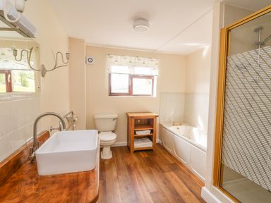 A bathroom with a wooden countertop sink toilet wooden shelf with towels bathtub and shower at Treboeth in Knighton