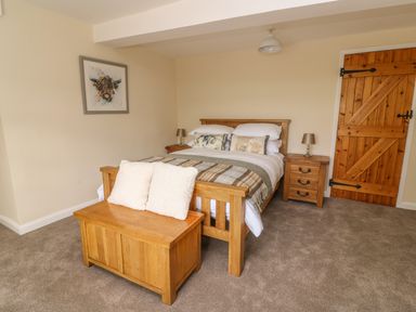 A bedroom with a wooden bed and bedside tables a wooden chest at the foot of the bed and a wooden door at Treboeth in Knighton