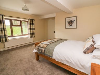A bedroom with a wooden bed, plaid curtains, a window overlooking grass, and a framed animal painting on the wall at Treboeth in Knighton