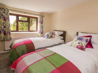 A bedroom with two single beds with white bedding and colorful blankets under a window with floral curtains at Treboeth in Knighton