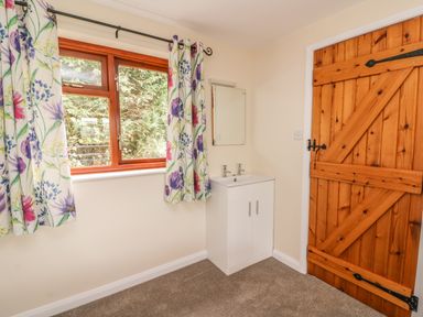 A room with a wooden door a white sink unit with a mirror and a window with floral curtains at Treboeth in Knighton