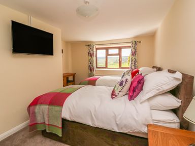 A bedroom with two beds a wall-mounted television and a window with floral curtains at Treboeth in Knighton
