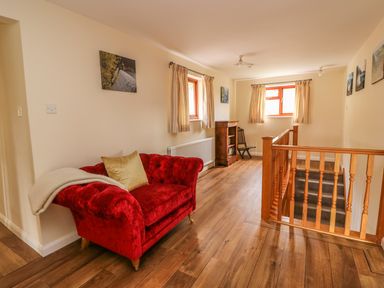 A seating area with a red sofa and a wooden bookcase near windows and a staircase with wooden railing at Treboeth in Knighton