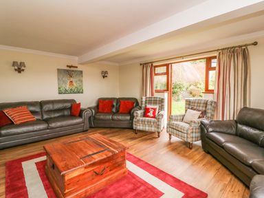 A living room with leather sofas plaid armchairs a wooden coffee table and a sliding door to a garden at Treboeth in Knighton