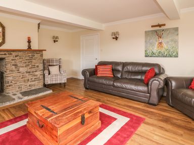 A living room with a brown leather sofa and armchair a wooden chest coffee table a stone fireplace and a painting of a rabbit at Treboeth in Knighton