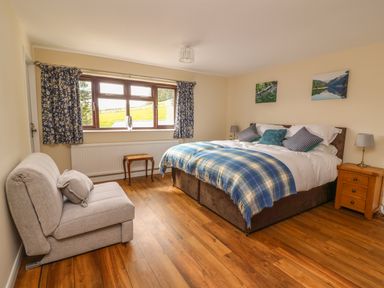 A bedroom with a double bed a small sofa a wooden stool wooden bedside tables and floral curtains at Treboeth in Knighton