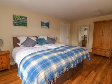 A bedroom with a double bed covered with a blue plaid blanket a wooden wardrobe a full length mirror and nightstands at Treboeth in Knighton