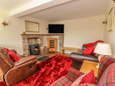 A living room with a stone fireplace TV and red rug at Treboeth in Knighton
