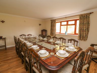 A dining room with a long wooden table set with plates bowls glasses and cutlery surrounded by wooden chairs at Treboeth in Knighton