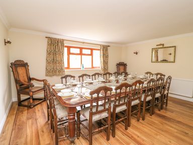A dining room with a long wooden table set with dishes and glasses surrounded by wooden chairs at Treboeth in Knighton