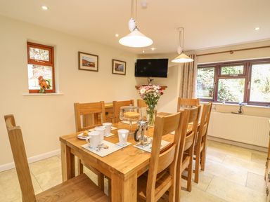 A dining room with a wooden table and chairs set with cups a cake and flowers at Treboeth in Knighton