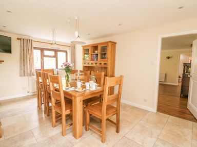 A dining room with a wooden table and chairs a cabinet with glass doors and a window with curtains at Treboeth in Knighton