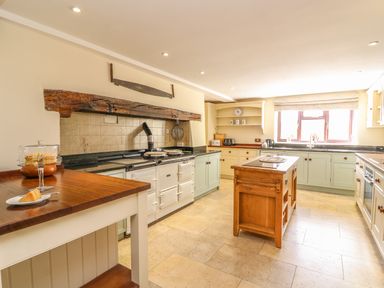 A kitchen with a wooden island a cake on a table and a large white stove under a wooden beam at Treboeth in Knighton
