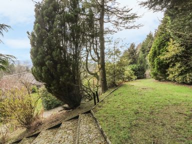 A garden area with grass trees and shrubs and a gravel path with steps at Treboeth in Knighton