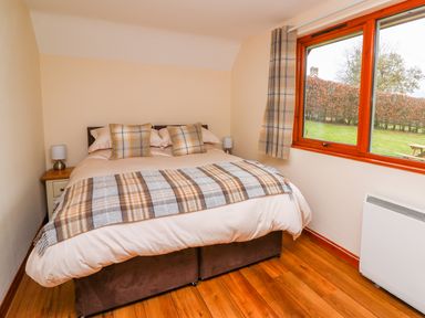 A bedroom with a bed two bedside tables two lamps a window and curtains at Pines Pitch in Knighton
