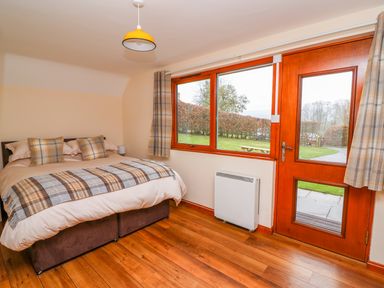 A bedroom with a double bed next to a window and a wooden door with glass panels at Pines Pitch in Knighton