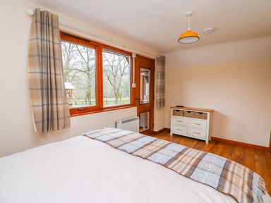 A bedroom with a bed covered with a plaid blanket a window with plaid curtains a door and a white dresser with wicker drawers at Pines Pitch in Knighton