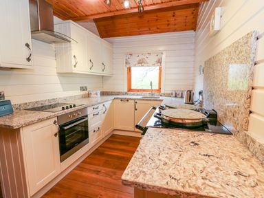 A kitchen with white cabinets a stovetop an oven a kettle and a window at Pines Pitch in Knighton