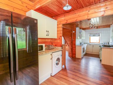 A kitchen with wooden floors wooden walls white cabinets a black refrigerator and a washing machine at Pines Pitch in Knighton
