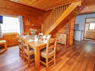 A dining area with a wooden table and six chairs set with cups and plates next to a wooden staircase at Pines Pitch in Knighton
