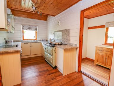 A kitchen with wooden floors white cabinets granite countertops and an oven next to a room with a wooden cabinet at Pines Pitch in Knighton