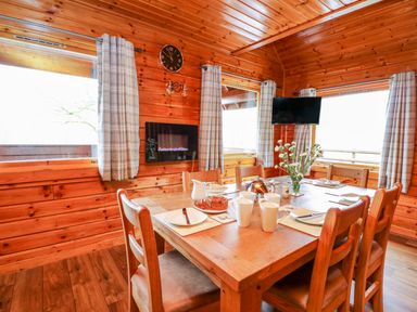 A wooden dining room with a table set for six people a clock on the wall and a mounted television at Pines Pitch in Knighton
